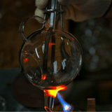 Artisan crafting a Manmaru glass teapot using traditional glassblowing techniques, showing the glowing molten glass being shaped by hand over an open flame.