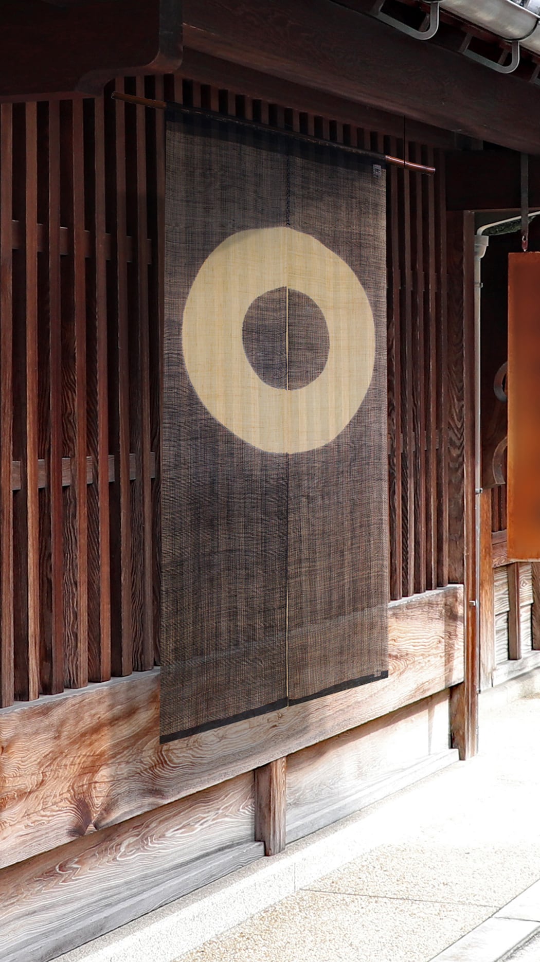 Janome noren curtain with concentric circle motif hanging in a traditional wooden Japanese entryway