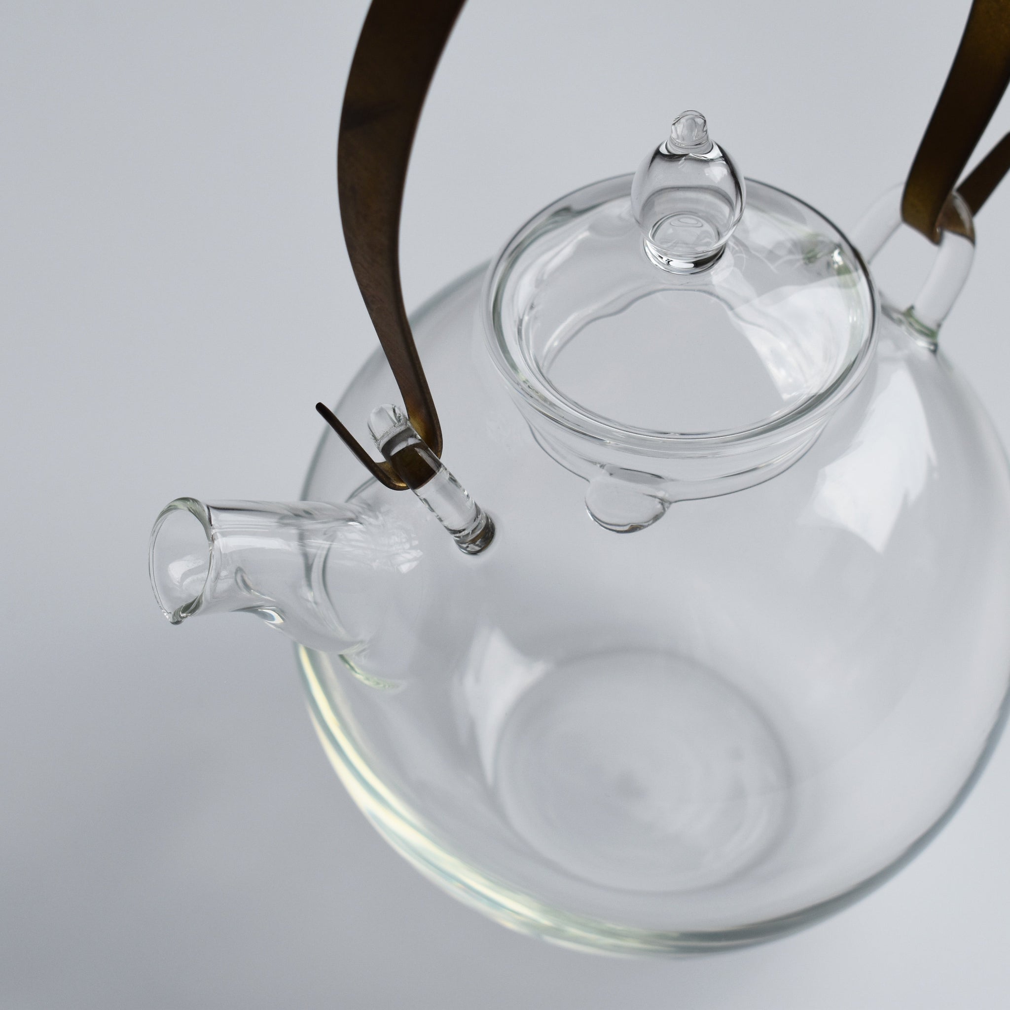 Close-up of the Manmaru glass teapot with a brass handle, showing the detailed spout, lid, and minimalist Japanese glass craftsmanship.