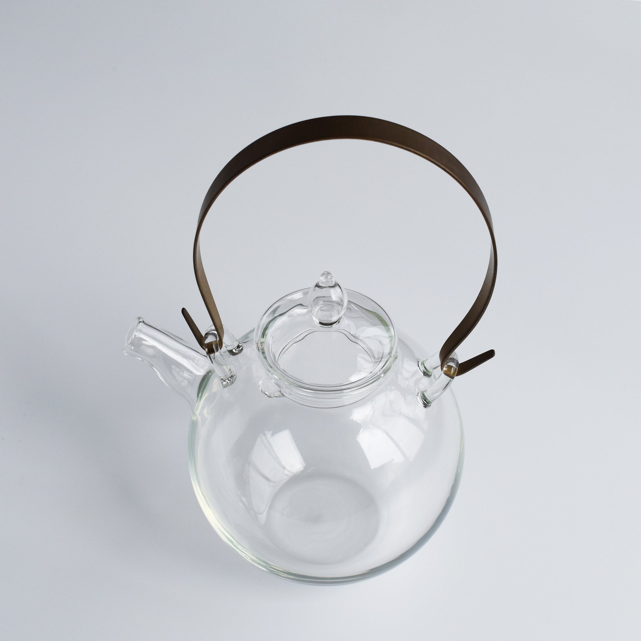 Top view of the Manmaru glass teapot with a sturdy brass handle, highlighting its minimalist Japanese craftsmanship and elegant round body.