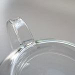Close-up view of the Manmaru glass teapot handle, showcasing the smooth and seamless craftsmanship of the transparent borosilicate glass.
