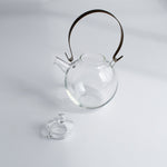 Manmaru glass teapot with a brass handle and its lid removed, showcasing its handcrafted Japanese design and minimalist aesthetic on a white background.