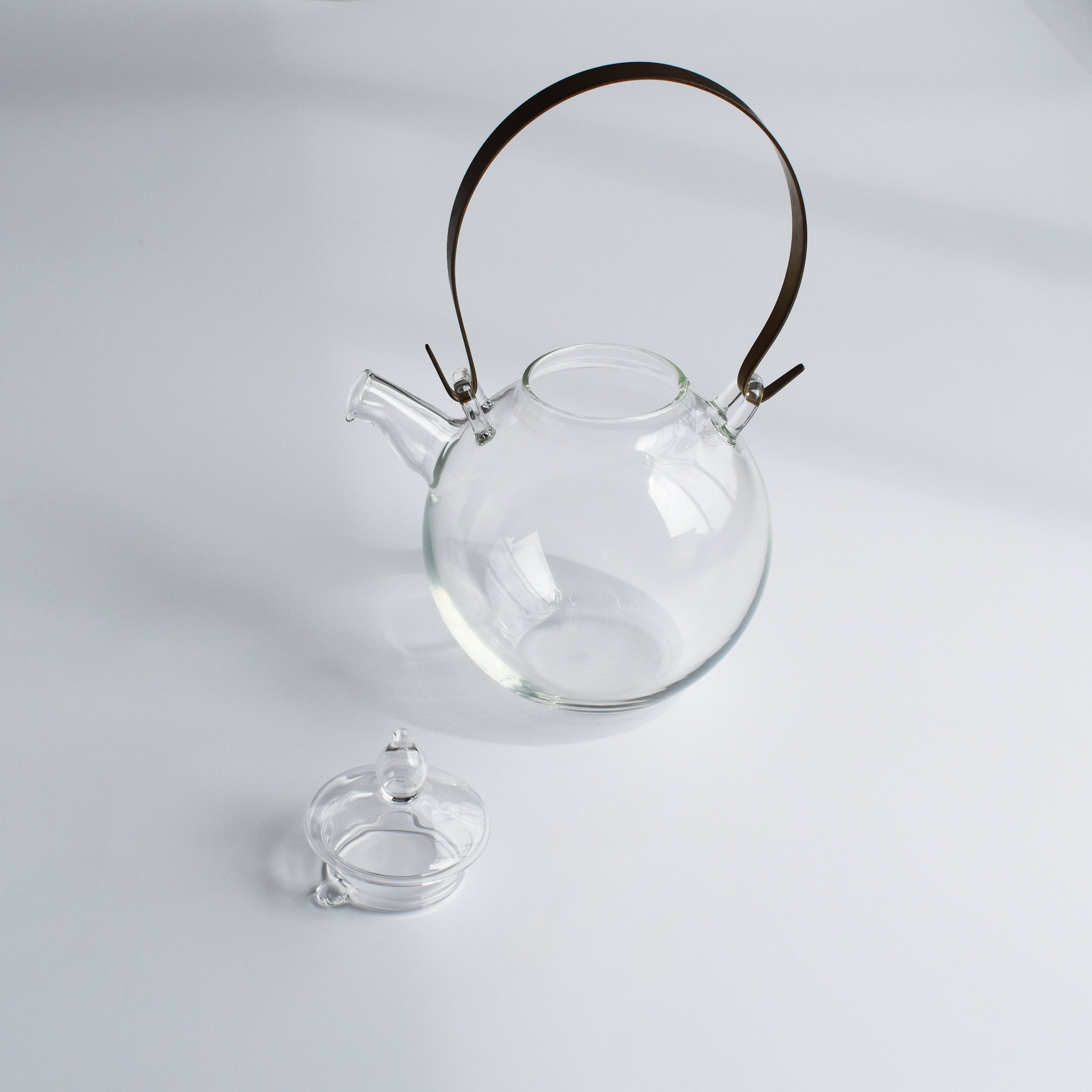 Manmaru glass teapot with a brass handle and its lid removed, showcasing its handcrafted Japanese design and minimalist aesthetic on a white background.