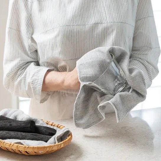 Using the Shirayuki Kitchen Cloth with Binchotan Charcoal to dry a glass, with Binchotan sticks displayed in a basket.