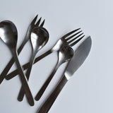 A set of Sori Yanagi stainless steel cutlery, including knives, forks, and spoons, arranged on a white surface, showcasing minimalist Japanese design and high-quality craftsmanship.