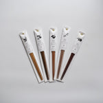 Set of five Tetoca Japanese wooden chopsticks in individual white paper sleeves, each with a botanical illustration and Japanese text, arranged in a fan shape on a light background.