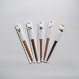 Set of five Tetoca Japanese wooden chopsticks in individual white paper sleeves, each with a botanical illustration and Japanese text, arranged in a fan shape on a light background.