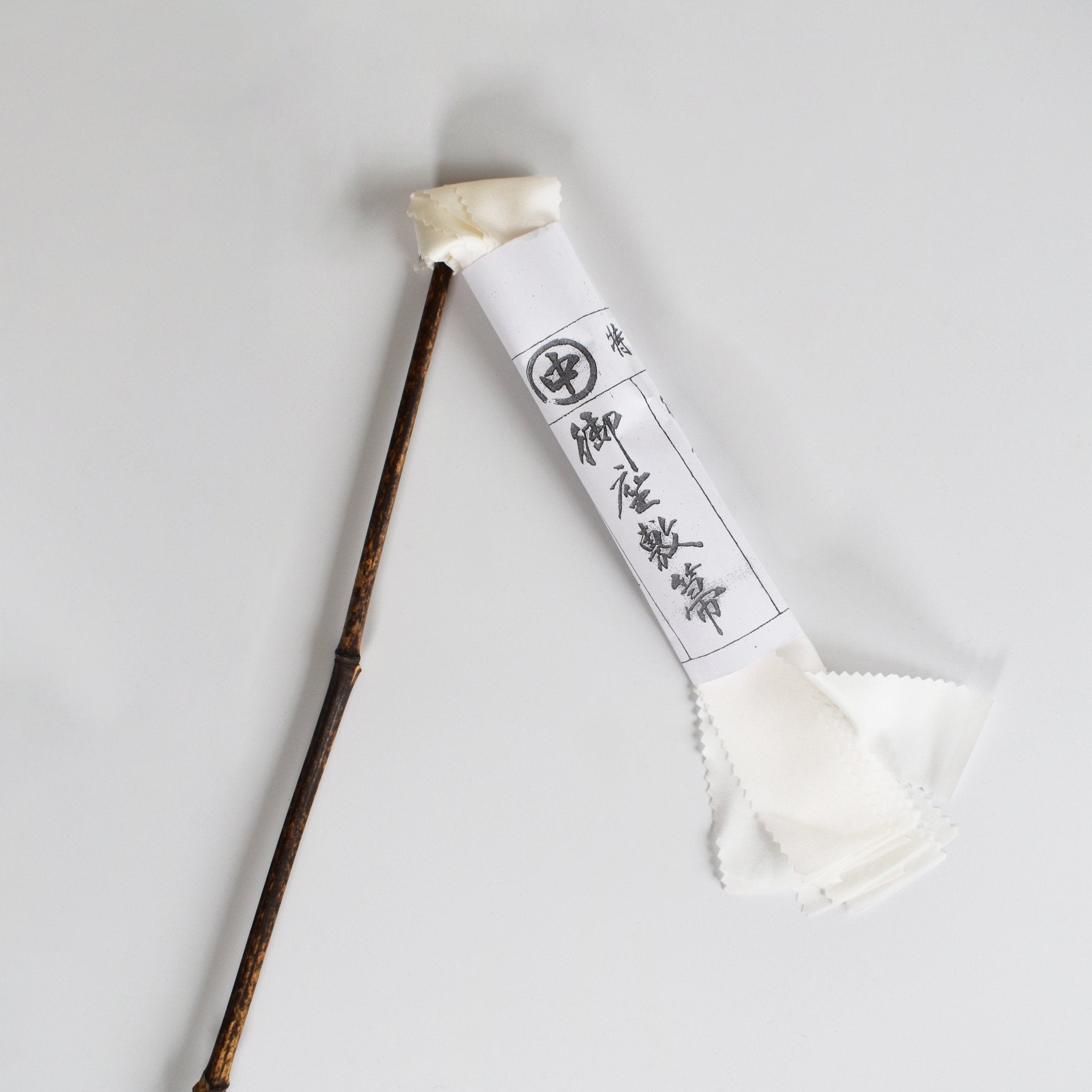 Traditional Japanese silk duster with a bamboo handle and white silk strips, shown with its paper wrapping featuring Japanese calligraphy.