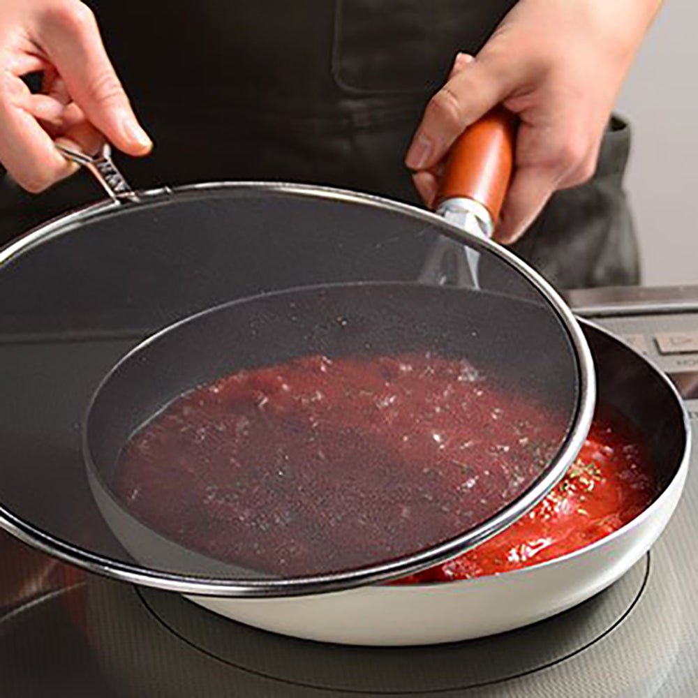 Placing the splatter screen over a pan of simmering tomato sauce to prevent oil and sauce splatters